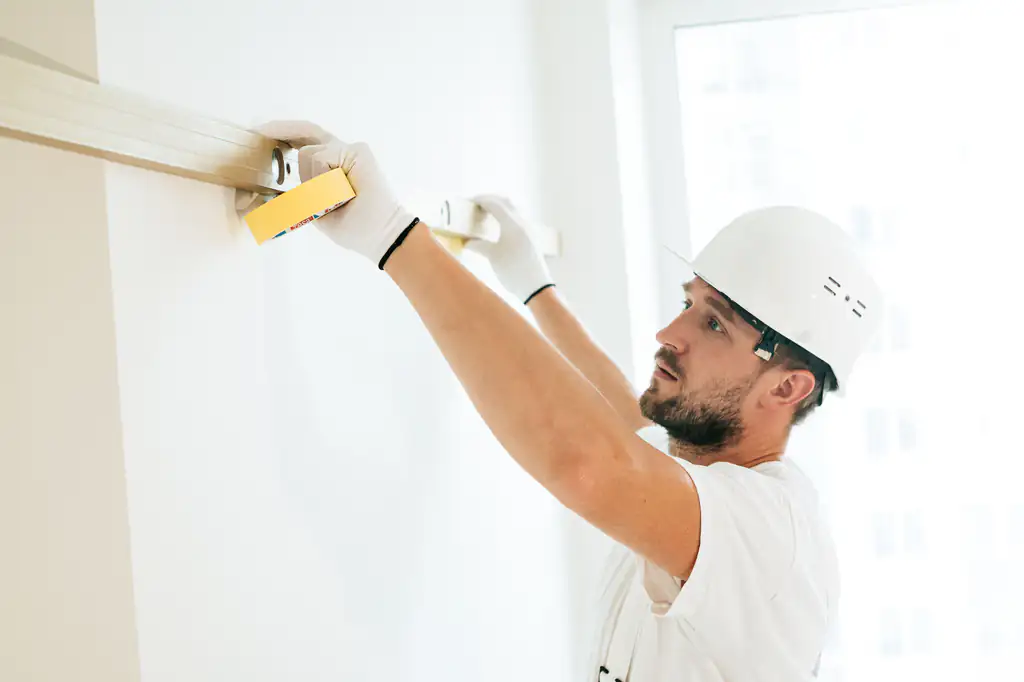 Tradesman in a hard hat checking a wall with a long spirit level