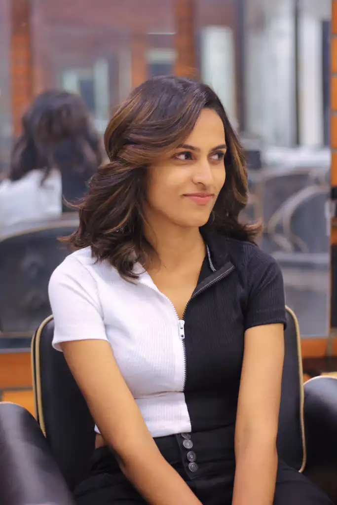 Woman in a salon chair with shoulder-length brown hair, warm balayage and a soft bend