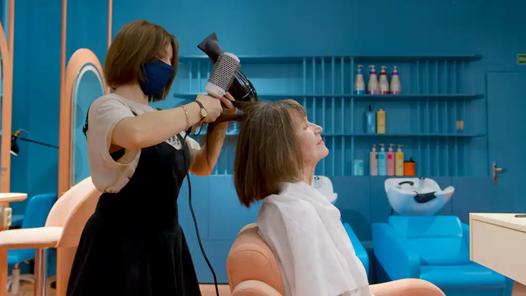 Stylist blow-drying a client's hair with a round brush in a teal-painted salon