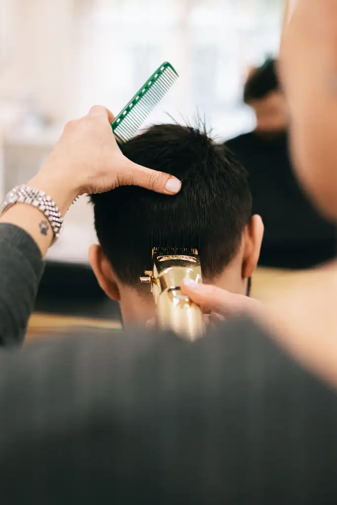 Close-up of clippers tidying the nape of a short dark crop, comb held above