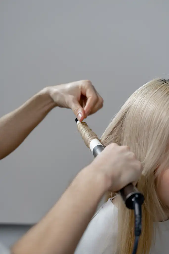 Stylist wrapping a section of pale blonde hair around a curling wand