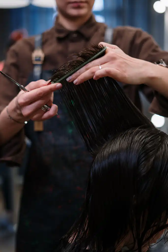 Stylist in an apron holding a section of wet hair flat with a comb before cutting